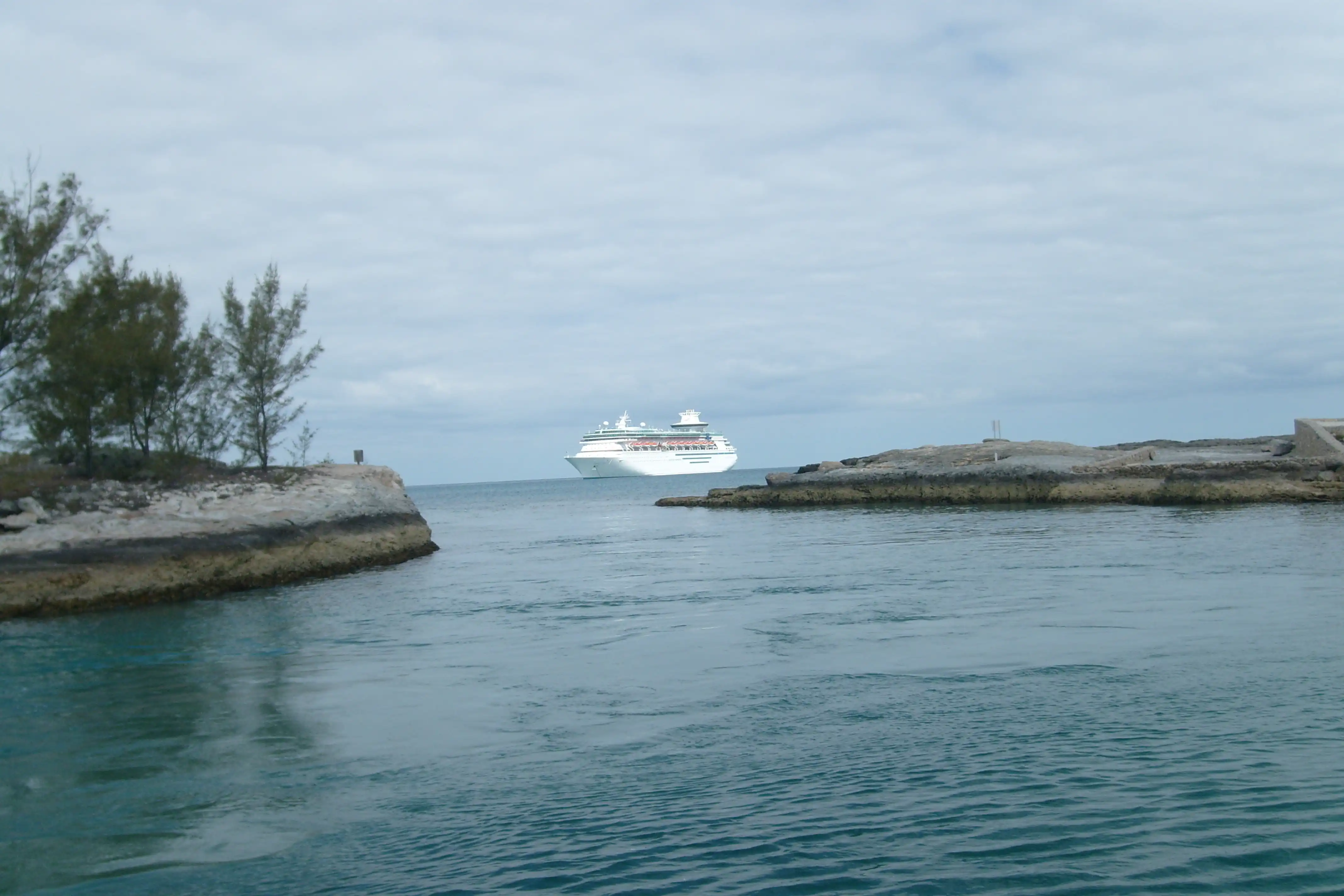 A small bay with a cruise ship on the ocean beyond it