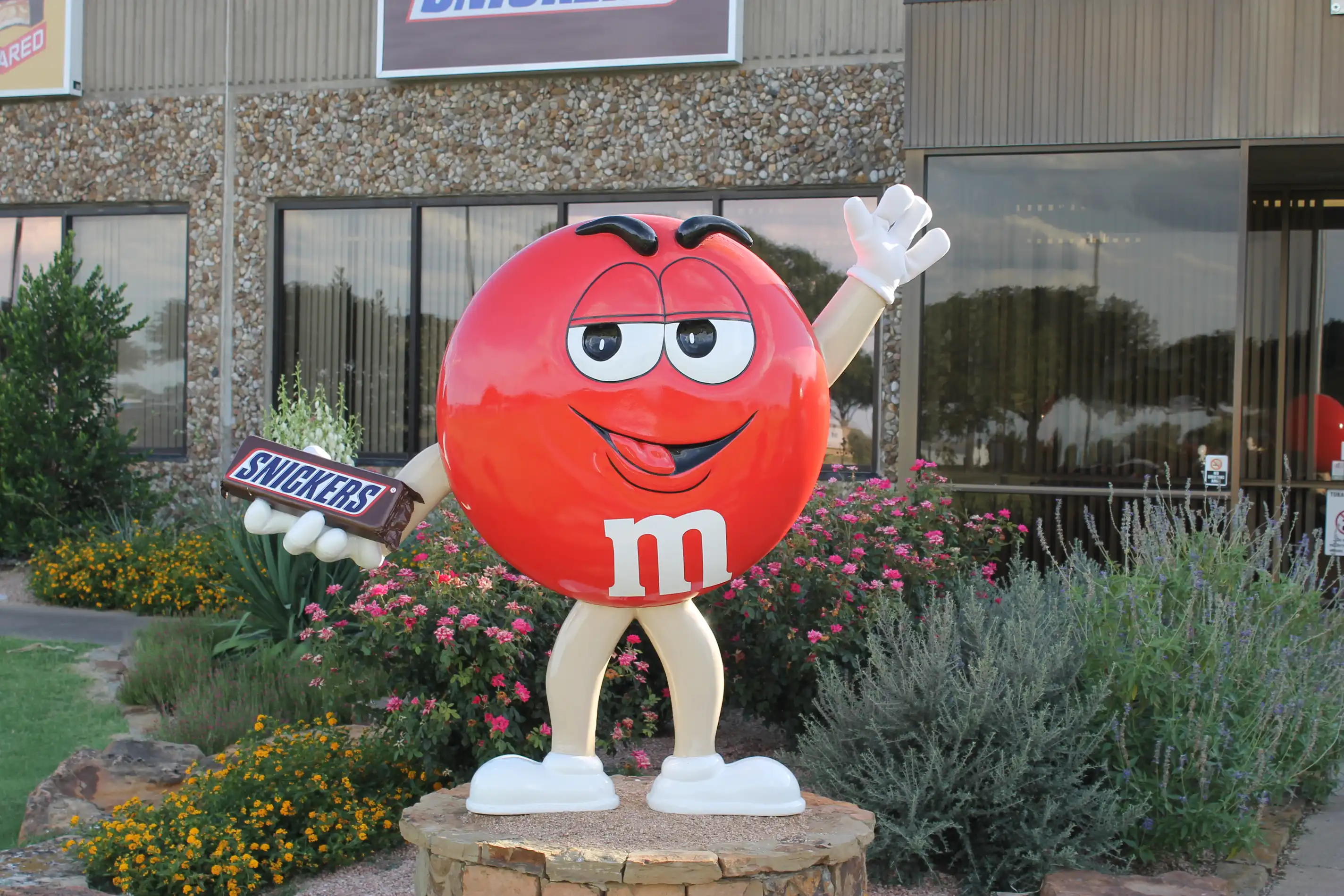 Statue of the red m & m person holding a snickers