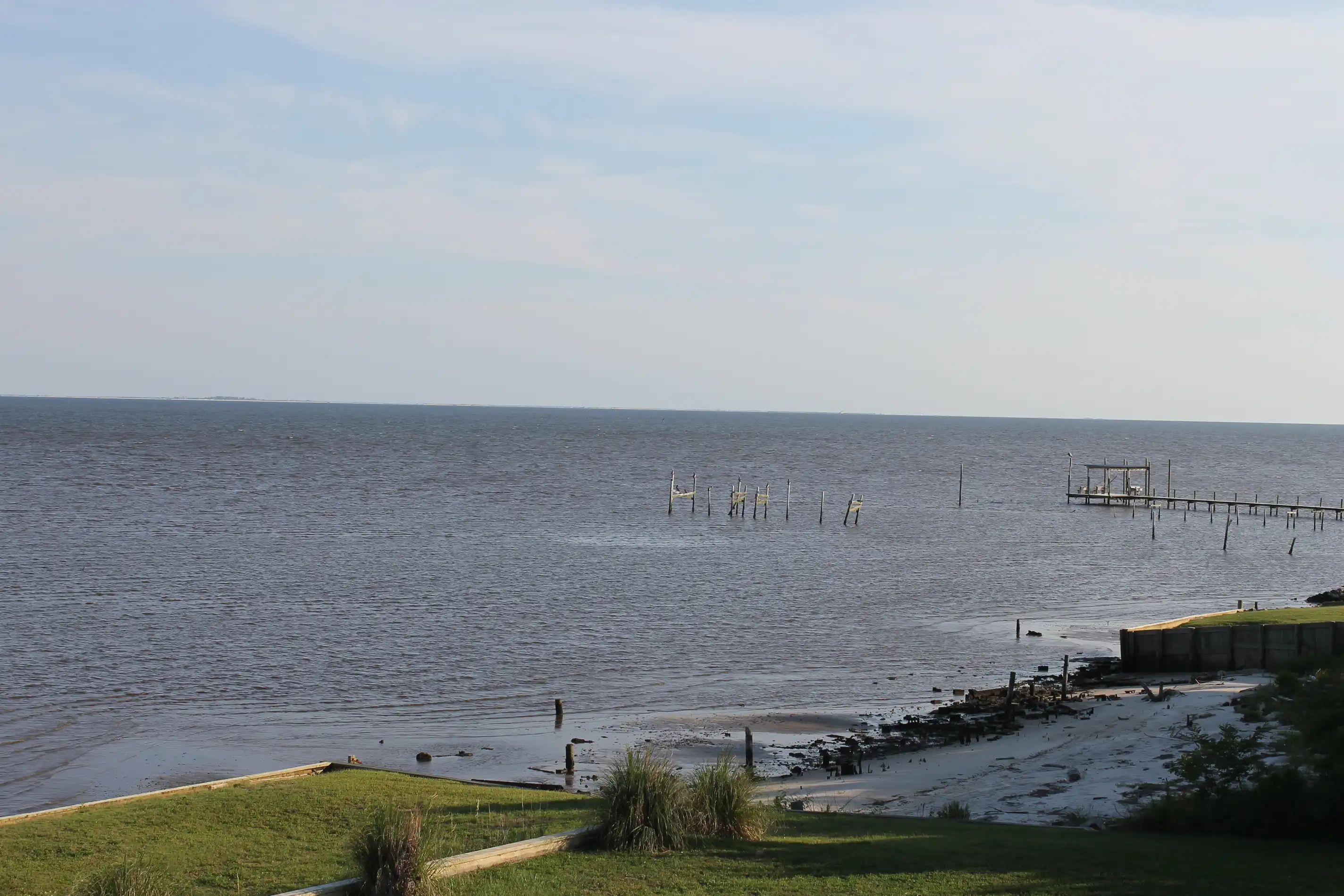 An ocean scene with a destroyed pier and a beach that is a mix of well manicured grassy areas and sandy areas