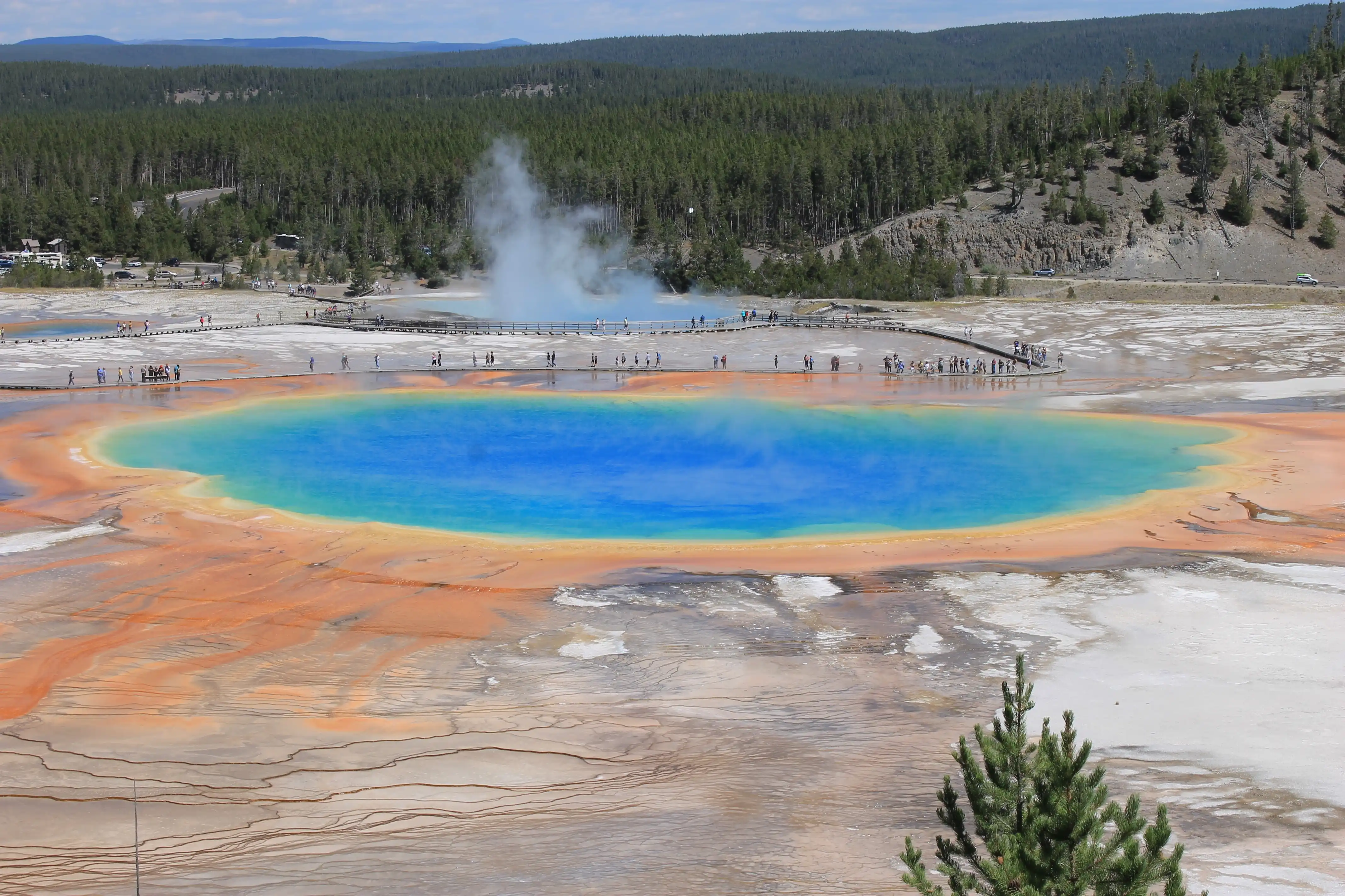 A small vibrant blue volcanic lake surrounded by clay and a walking path