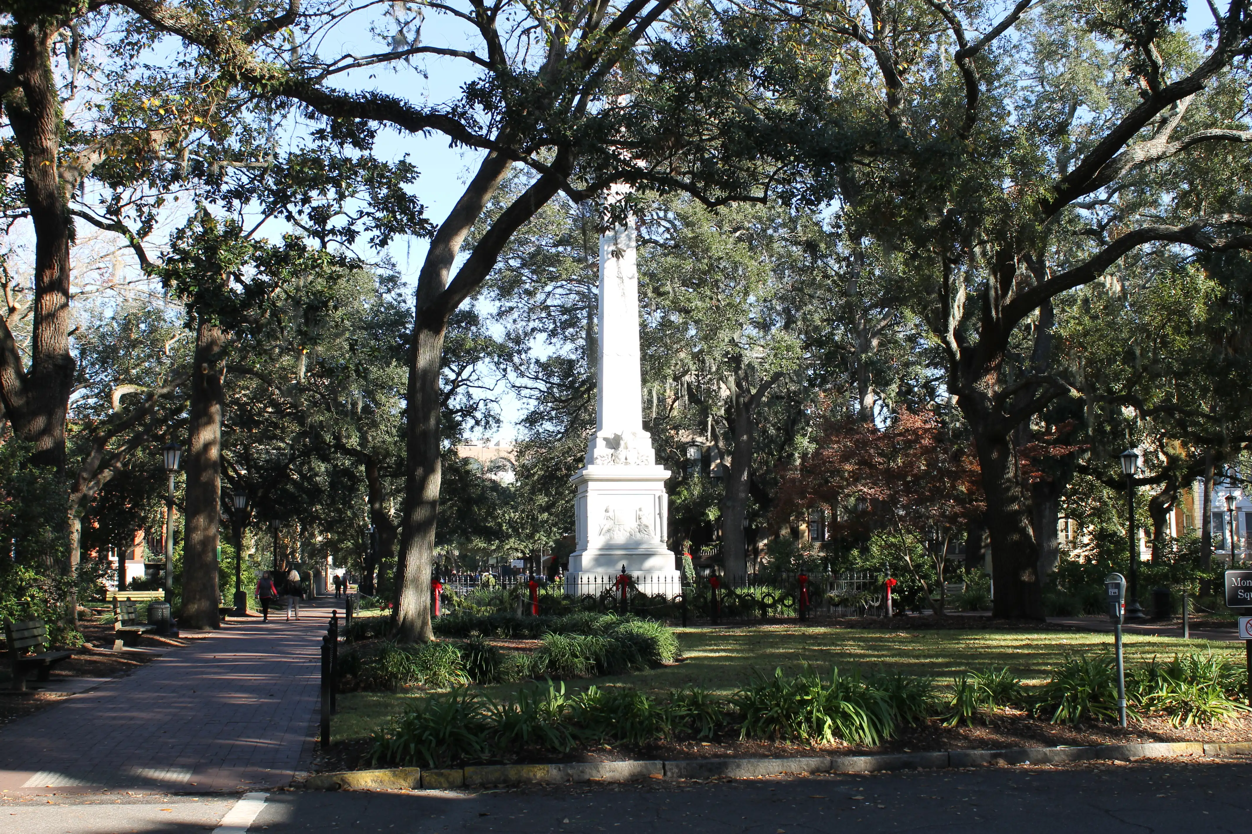 A monument standing in the middle of a tree filled park with christmas garland wrapped around its fencing