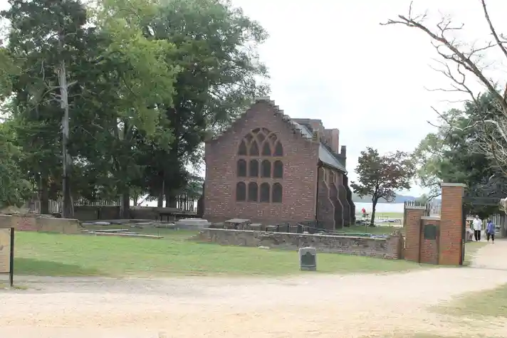 A very old brick church with a small graveyard and a lake in the backdrop